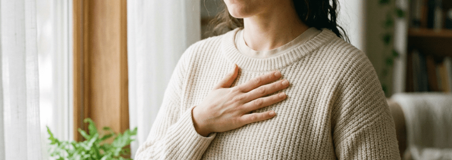 Woman practicing mindfulness meditation with hands on chest and stomach by window